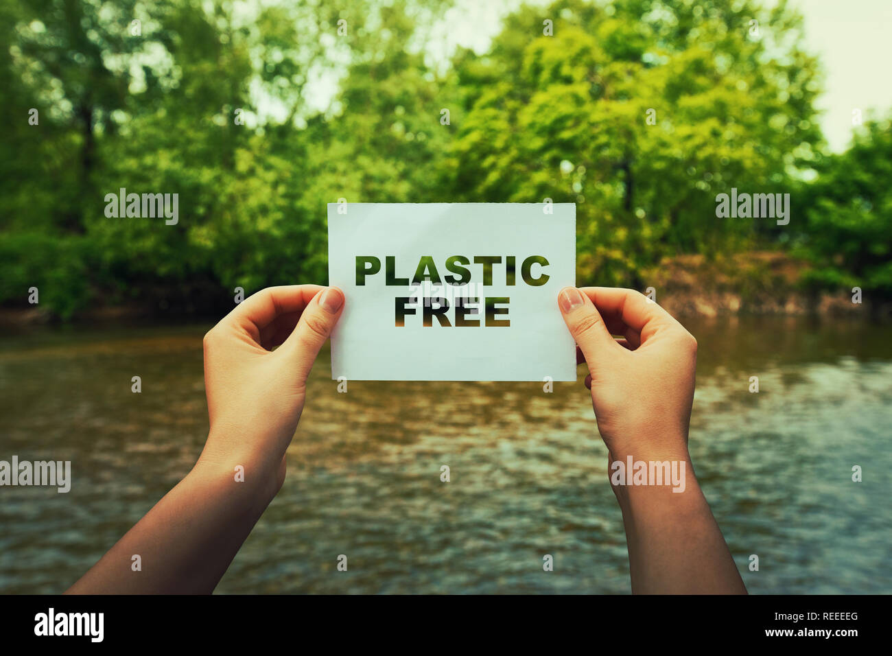 Frau Hände halten ein Blatt Papier mit Kunststoff freier Text mitten in der Natur in der Nähe eines fließenden Fluss und grüne Wälder. Ökologie Konzept, s Recyceln Stockfoto