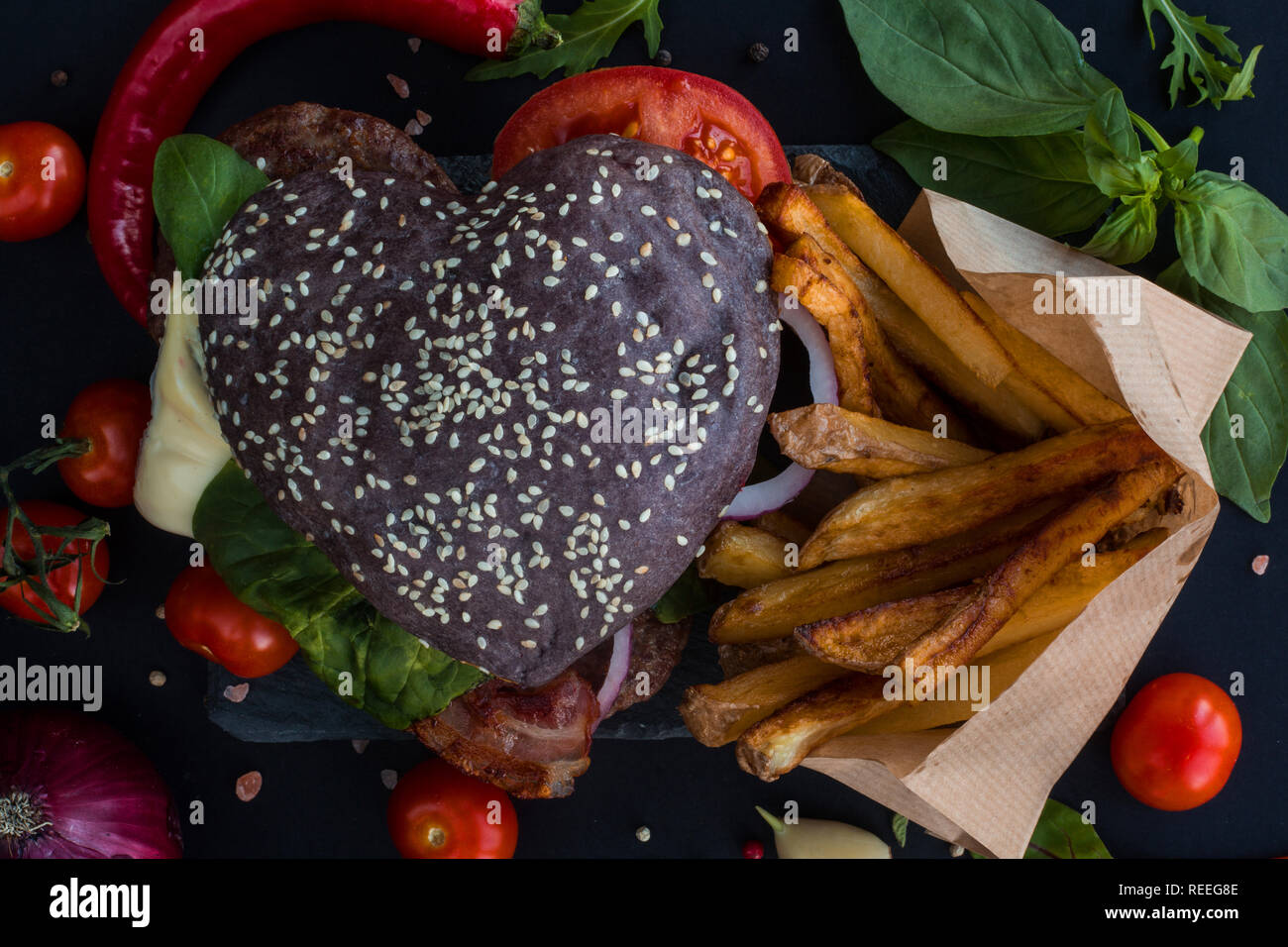 Herzförmige schwarz Hamburger und Pommes frites auf der Steinplatte, liebe Burger fast food Konzept, Valentinstag Überraschung zum Abendessen, Holz- Hintergrund, oben vi. Stockfoto