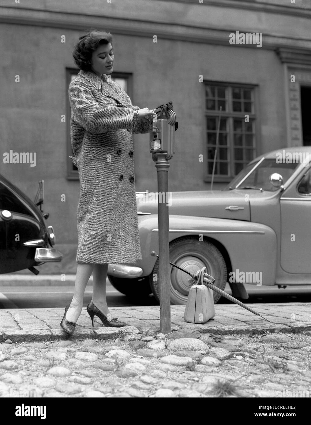 Mode in den 50er Jahren. Eine junge Frau trägt eine typische 50er Jahre Herbst Mode Mantel. Sie zahlt für Ihr Ticket in die parkuhr in einer Straße. Schweden 1950. Foto Kristoffersson Ref321 a-5 Stockfoto