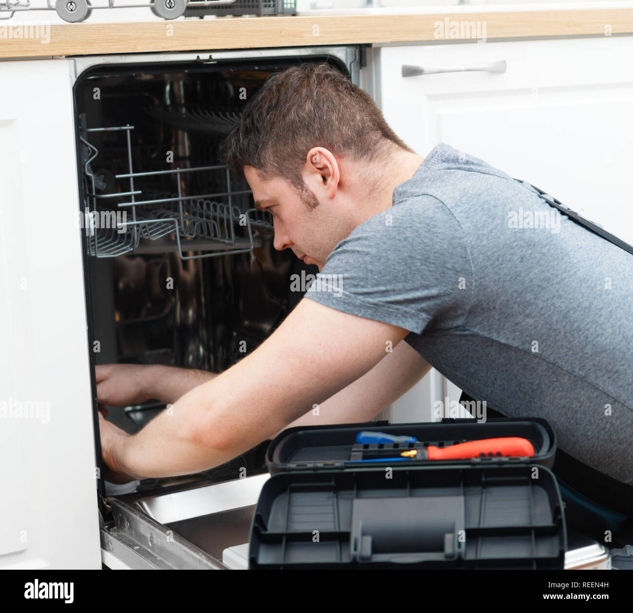 Professionelle Handwerker in Latzhosen Instandsetzung der inländischen Geschirrspüler in der Küche. Stockfoto