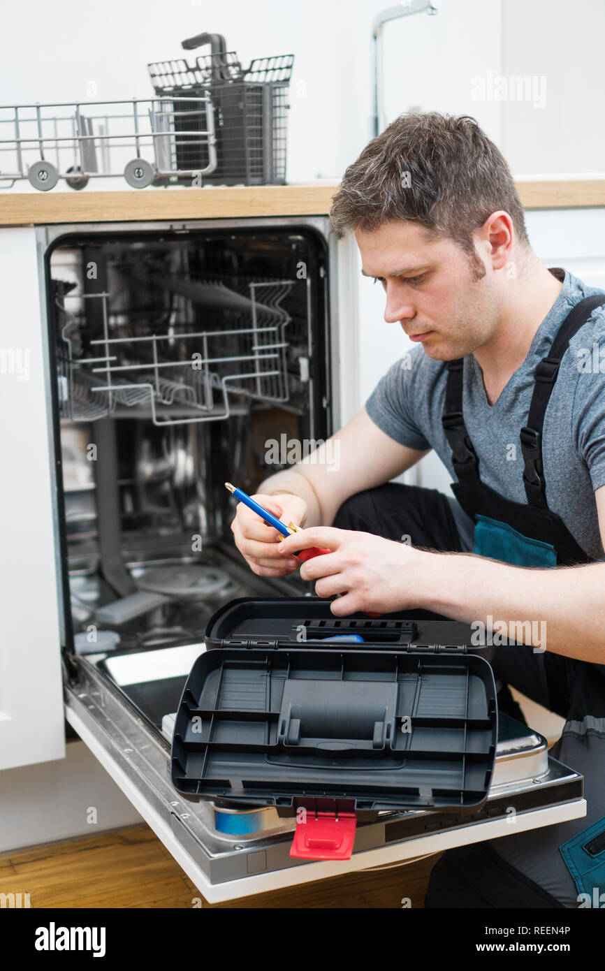 Professionelle Handwerker in Latzhosen Instandsetzung der inländischen Geschirrspüler in der Küche. Stockfoto