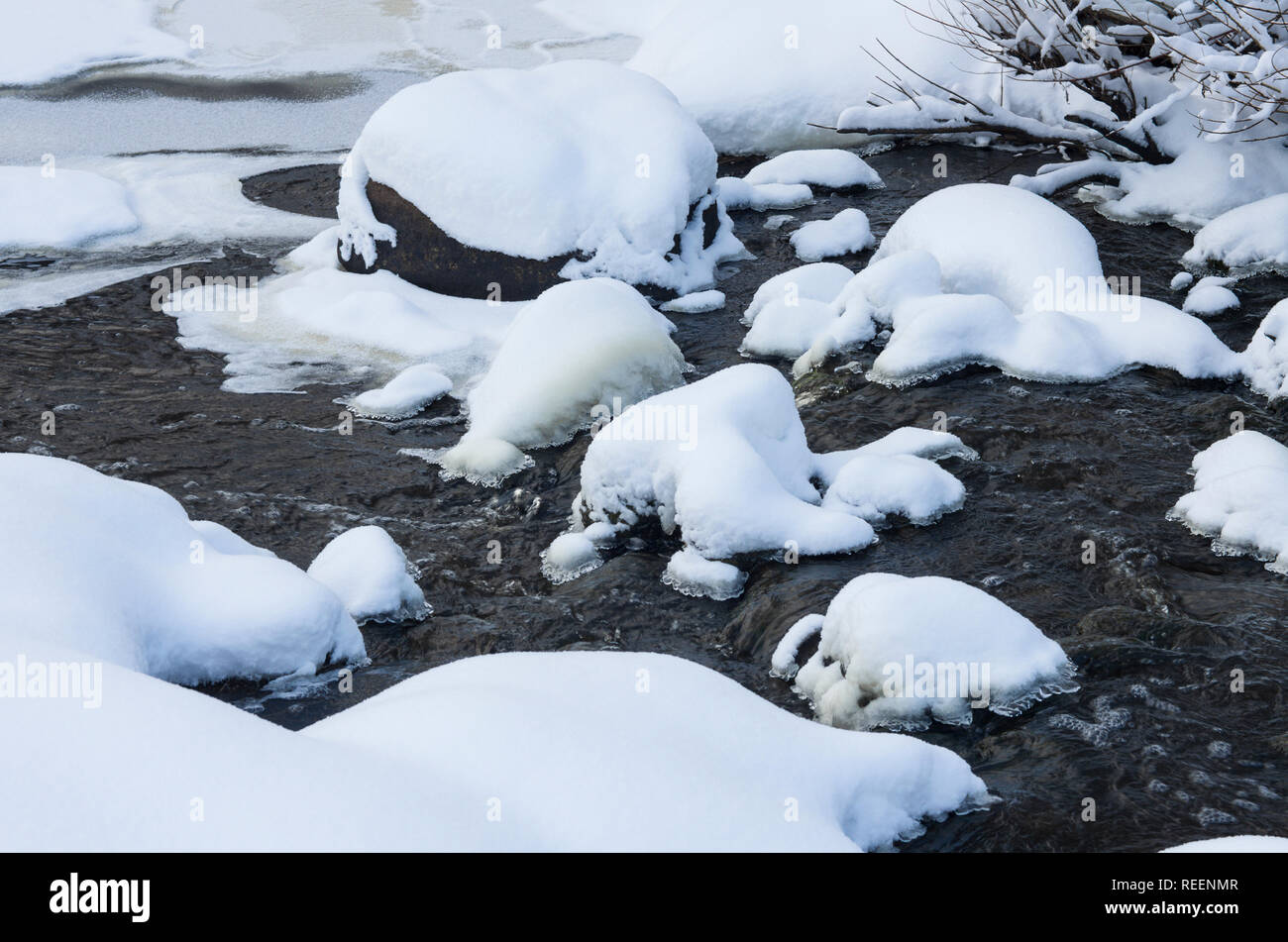 Schnee-bedeckten Steine und Banken mit Eis Kante in der turbulenten Strömung des Flusses an einem bewölkten Tag Stockfoto