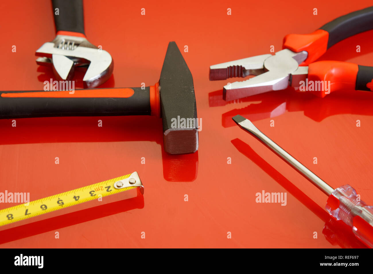 Zangen, Maßband, Schraubendreher, Hammer und verstellbarer Schraubenschlüssel liegen auf einem roten polierte Oberfläche. Werkzeuge für die Mechaniker. Stockfoto