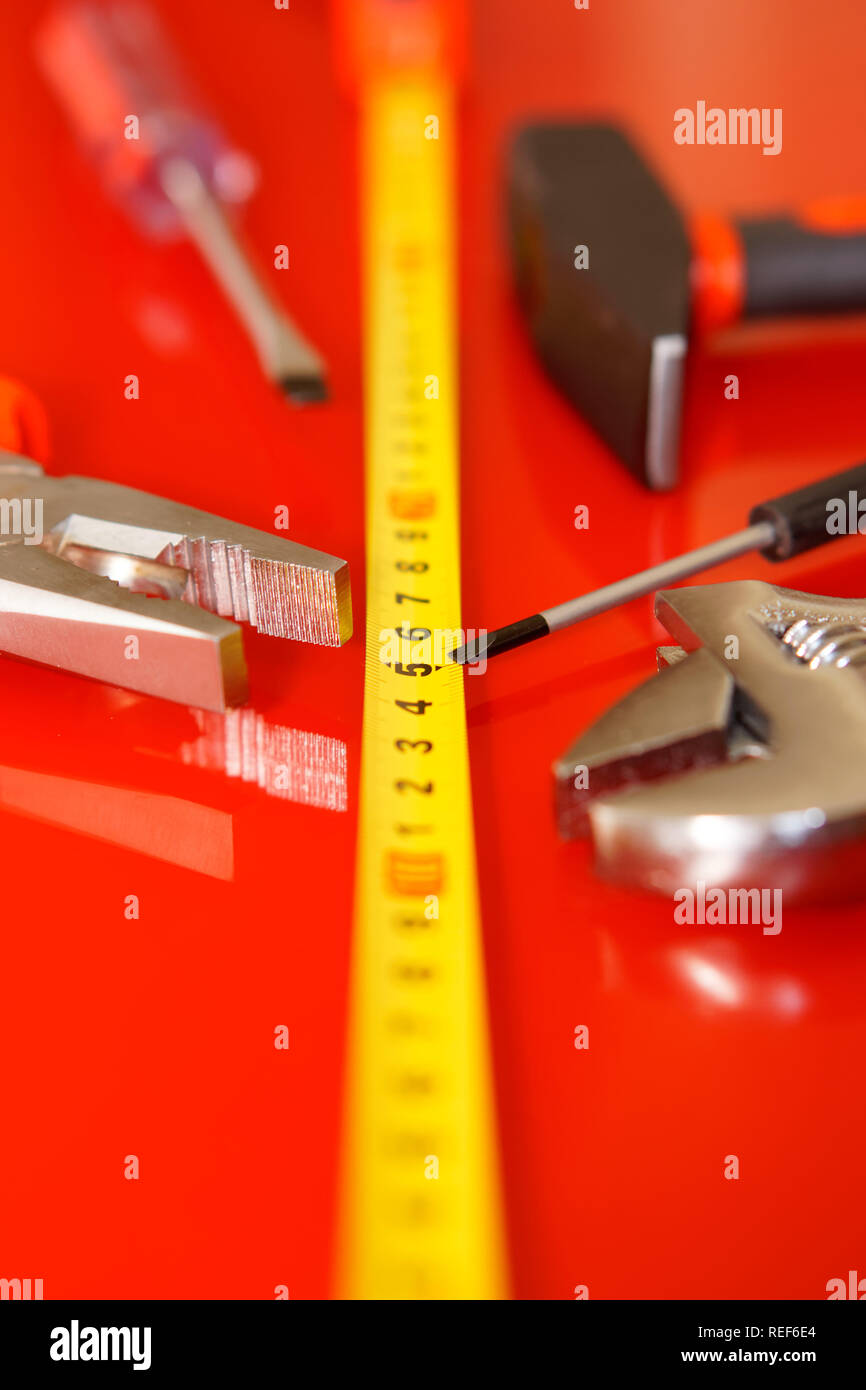 Schraubendreher, Zangen, Maßband, Hammer und verstellbarer Schraubenschlüssel liegen auf einem roten polierte Oberfläche. Werkzeuge für die Mechaniker. Geringe Tiefenschärfe. Vertica Stockfoto