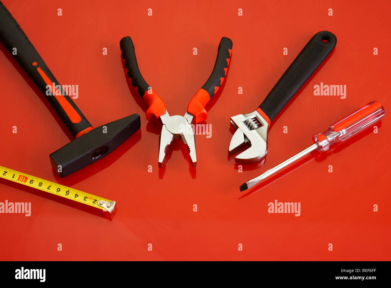 Hammer, Schraubendreher, Zangen, Maßband und verstellbarer Schraubenschlüssel liegen auf einem roten polierte Oberfläche. Werkzeuge für die Mechaniker. Stockfoto