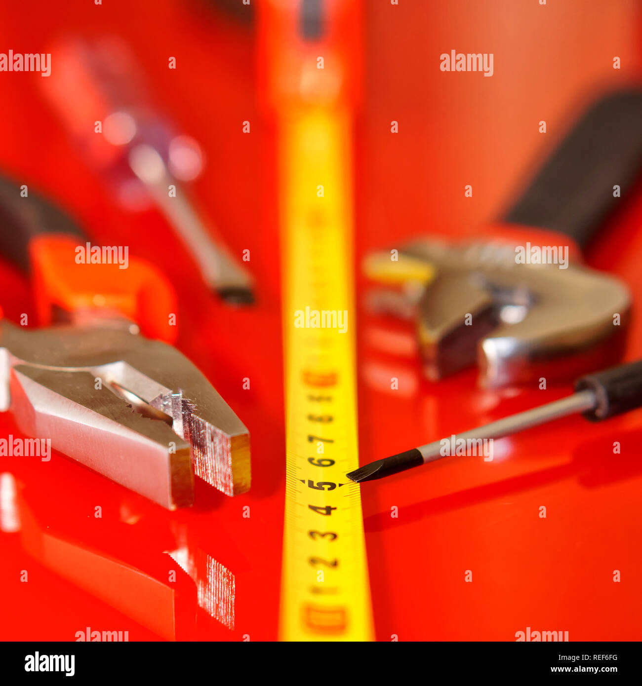 Maßband, Hammer, Schraubendreher, Zangen, und verstellbarer Schraubenschlüssel liegen auf einem roten polierte Oberfläche. Werkzeuge für die Mechaniker. Geringe Tiefenschärfe. Squar Stockfoto