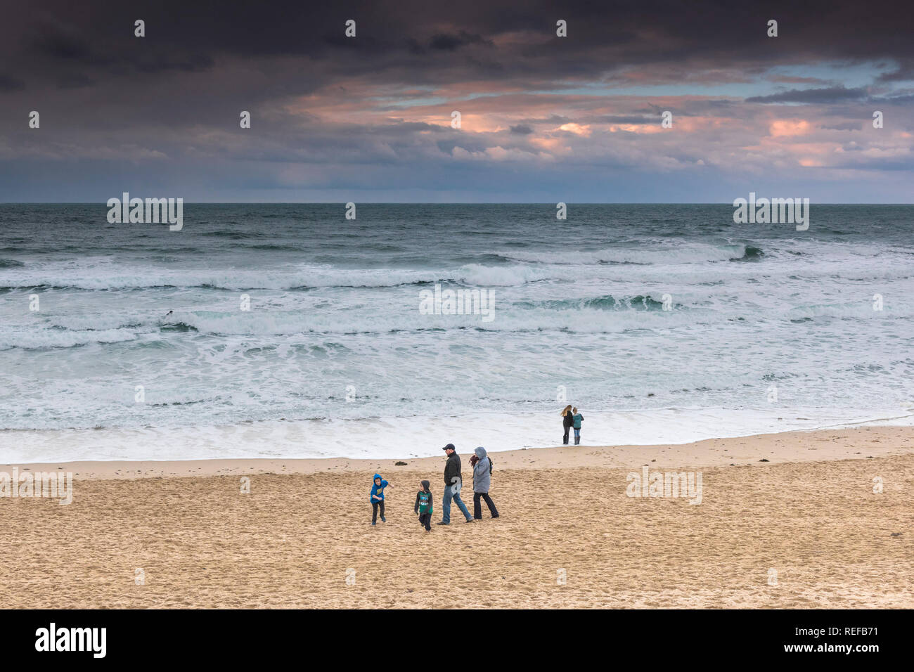 Schöne pastell Farben in den Himmel, wie die Sonne über Menschen zu Fuß entlang Fistral Beach in Newquay Cornwall. Stockfoto