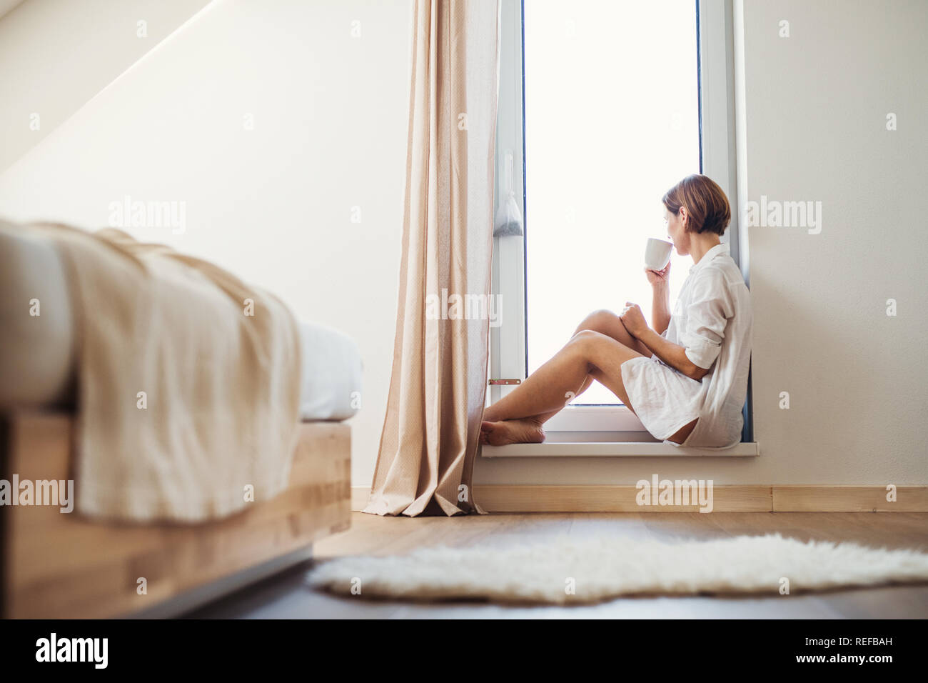 Eine junge Frau mit Nachthemd sitzen durch das Fenster in den Morgen. Stockfoto