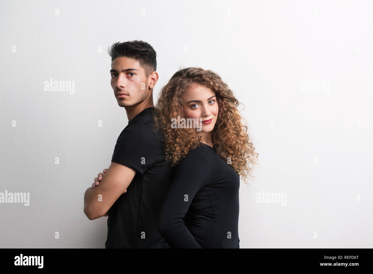 Porträt eines jungen Paares Rücken an Rücken in einem Studio, das Tragen von schwarzer Kleidung. Stockfoto