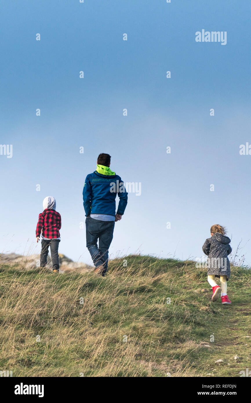 Ein Vater und seine zwei Kinder gehen auf einem Hügel in der Landschaft. Stockfoto