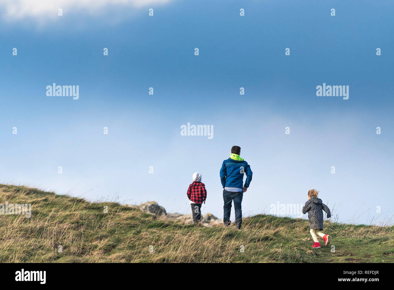 Ein Vater und seine zwei Kinder gehen auf einem Hügel in der Landschaft. Stockfoto