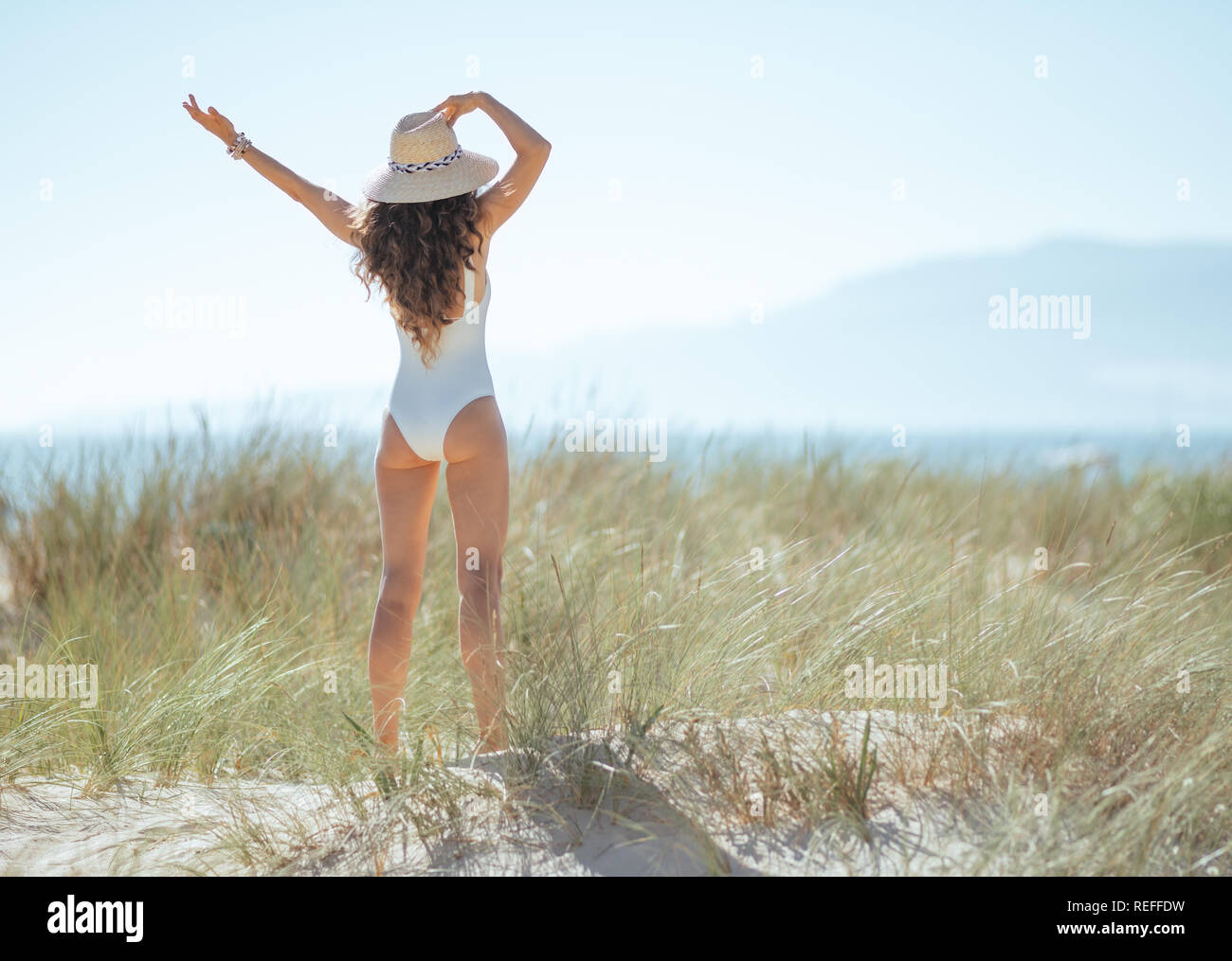 Hinter der jungen Frau in Weiß beachwear am Strand gesehen freuen. waring Frau Stroh Hut für Sonnenschutz. Ruhige Ferienhäuser Himmel. Europäischen wom Stockfoto Hinter der jungen Frau in Weiß beachwear am Strand gesehen freuen. waring Frau Stroh Hut für Sonnenschutz. Ruhige Ferienhäuser Himmel. Europäischen wom Stockfoto