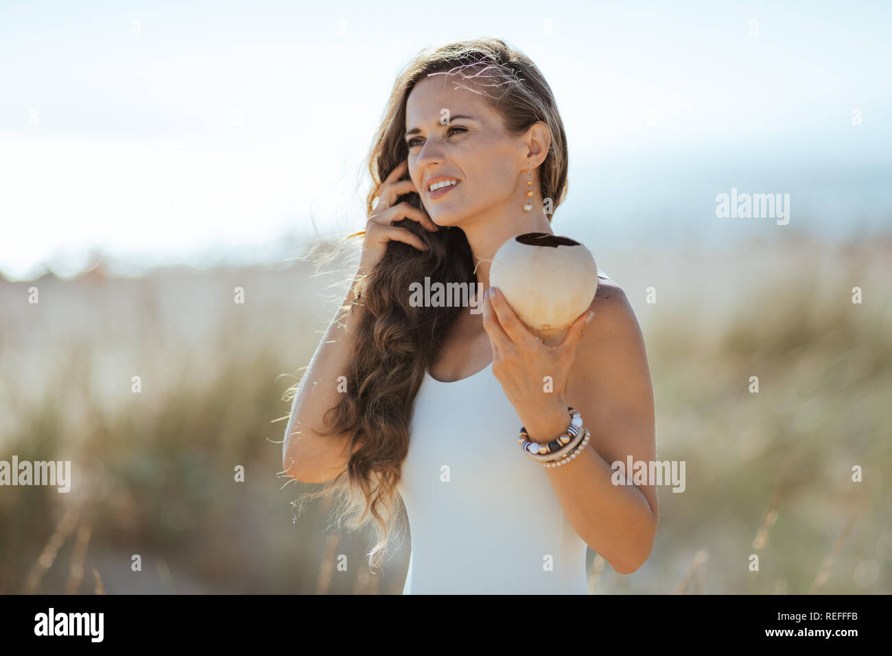 Junge Frau in weißen Badeanzug mit Kokosnuss auf das Meer. Kokosöl Haar vor Sonne zu schützen. Ruhige Ferienhäuser Himmel. Minimale bis keine Stockfoto Junge Frau in weißen Badeanzug mit Kokosnuss auf das Meer. Kokosöl Haar vor Sonne zu schützen. Ruhige Ferienhäuser Himmel. Minimale bis keine Stockfoto