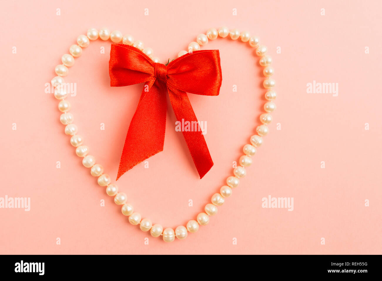 Weiße Perle Schmuck Herz Form mit roter Schleife auf rosa Hintergrund, flach Stil Stockfoto