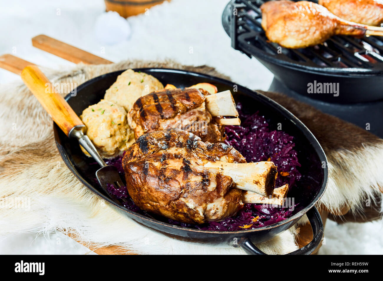 Lecker saftig marinierten Schweinefleisch vom Grill Sprunggelenk mit Klößen und Rotkohl für einen Winter Barbecue in einer Pfanne auf Schnee serviert. Stockfoto