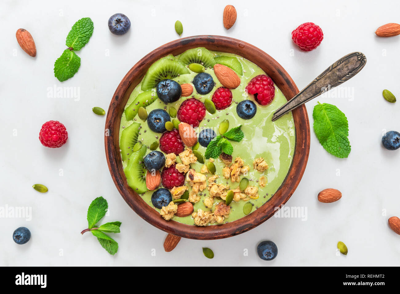 Schüssel mit Matcha Grüntee Smoothie mit frischen Beeren, Nüsse, Samen und Hafer Müsli mit einem Löffel für gesunde vegane, vegetarische Ernährung Frühstück. nach oben anzeigen. Stockfoto