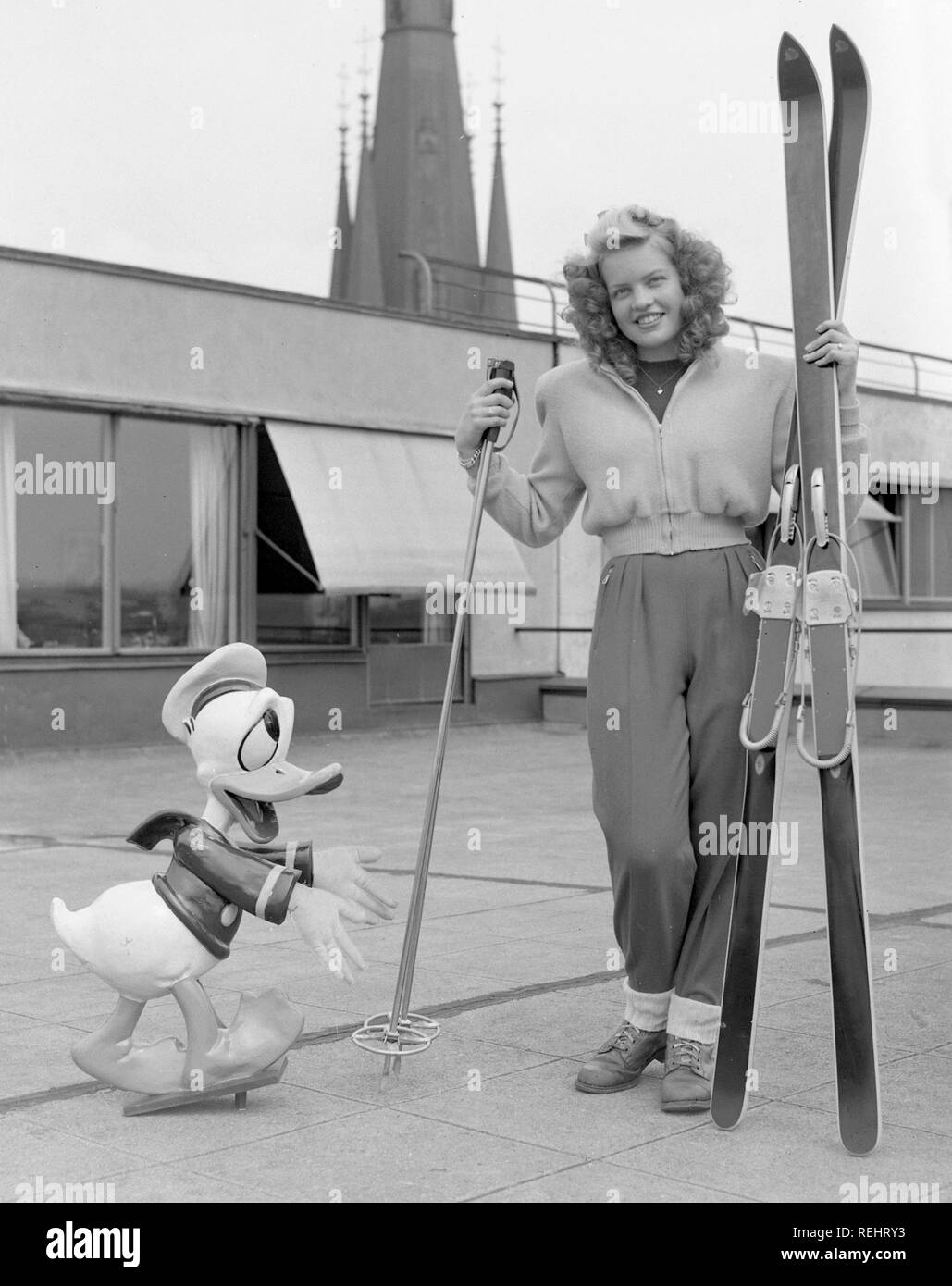 Wintersport in den 1950er Jahren. Eine junge blonde Frau mit ihrem Ski, Stöcke und Schuhe zusammen mit einem Donald Duck Figur. Schweden 1952. Foto Kristoffersson Ref 179 A-1 Stockfoto