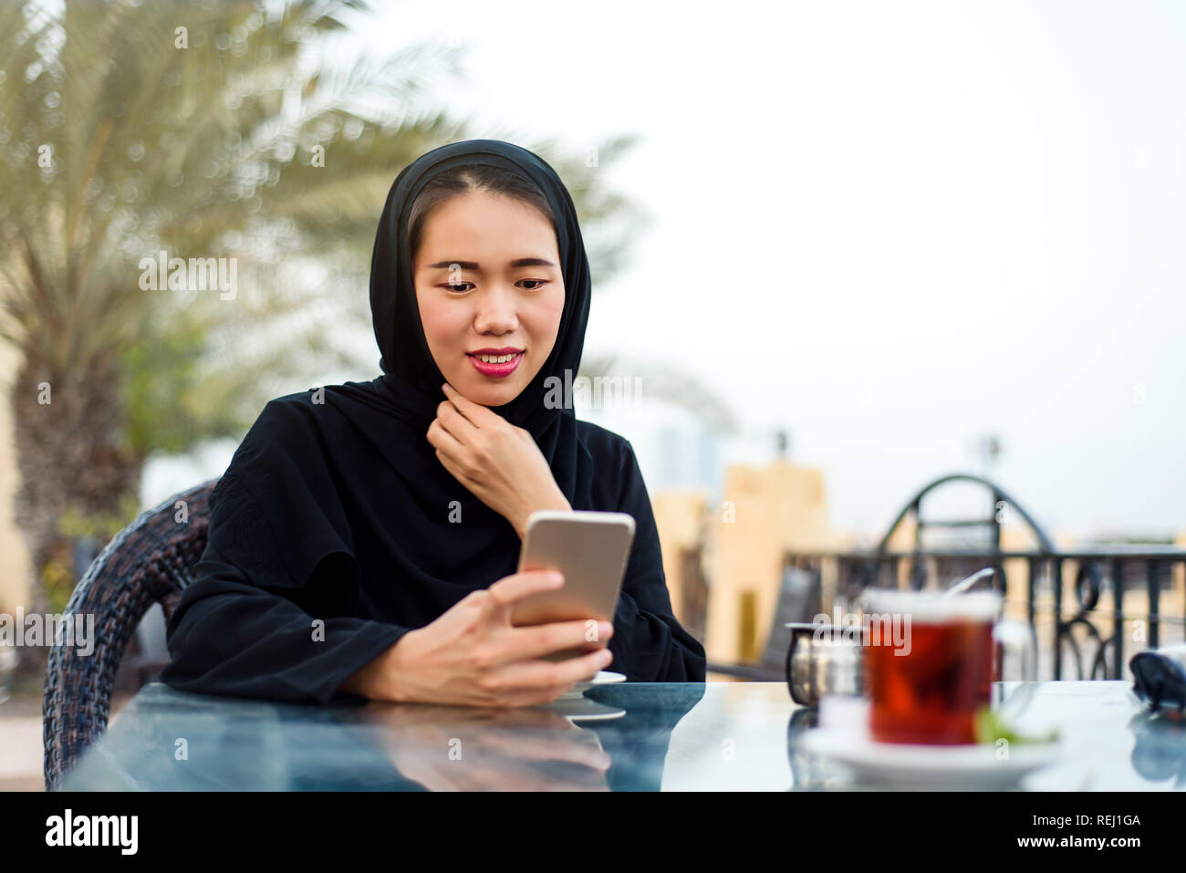 Muslimische Frau mit Phone bei einer Tasse Kaffee im Freien Stockfoto