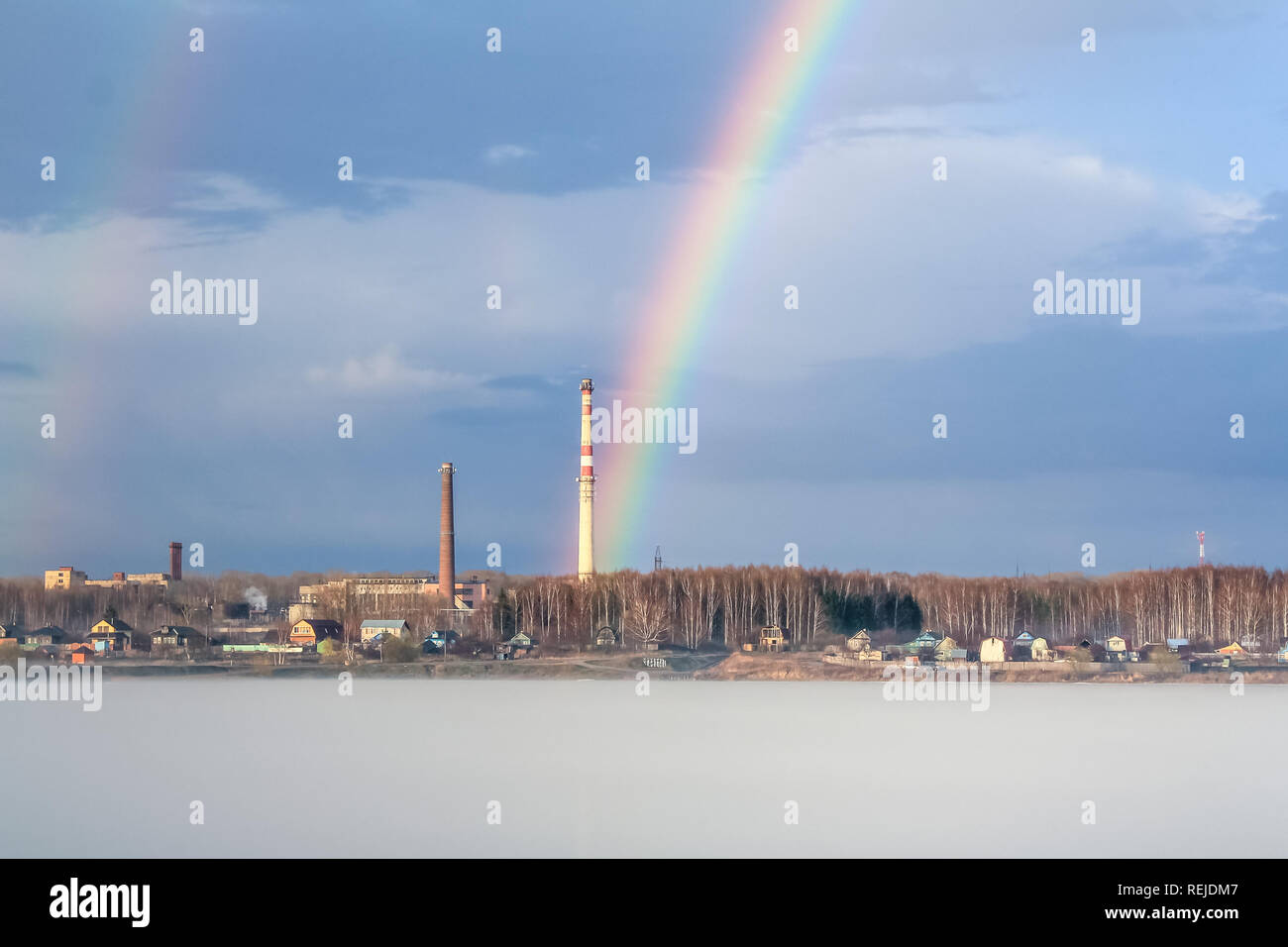 Friedlichen Frühling neblige Landschaft bei Sonnenaufgang nach dem Regen mit Regenbogen auf dem Fluss, im Hintergrund Industrieanlagen mit Rohr Stockfoto