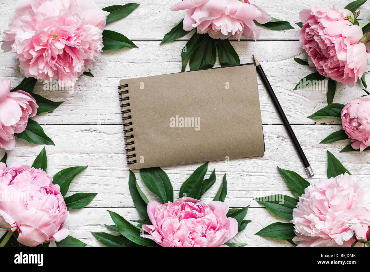 Leere vintage Papier Notebook im Rahmen von Pink peony Blumen über weiße Holztisch mit Kopie Platz gemacht. Blüte Zusammensetzung. top anzeigen. Flach. Natu Stockfoto