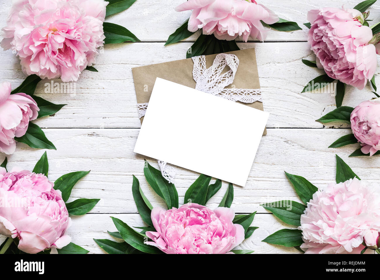 Leere Grußkarte iand Umschlag im Rahmen der rosa Pfingstrose Blüten über weiße Holztisch mit Kopie Raum. hochzeit einladung. top anzeigen. Flach. Stockfoto