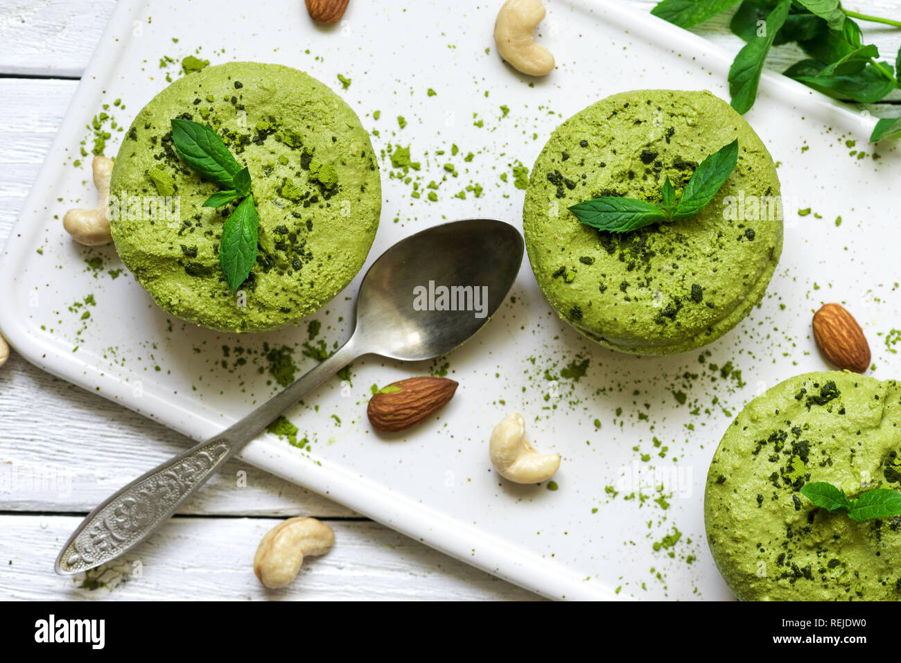 Green Matcha und Banane vegan rohe Kuchen mit Minze und Muttern über weiße Holztisch mit einem Löffel. Gesunde leckeres Essen. top View Stockfoto