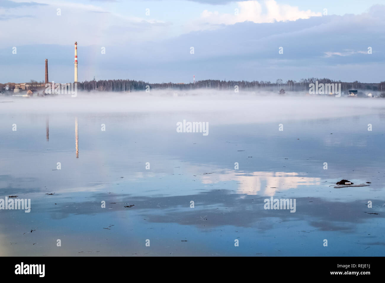 Friedlichen Frühling neblige Landschaft bei Sonnenaufgang nach dem Regen mit Regenbogen auf dem schmutzigen Fluss, im Hintergrund Industrieanlagen mit Rohr Stockfoto