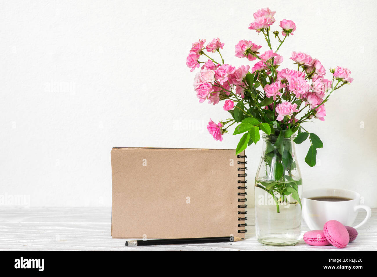 Kreative mock up mit einem schönen Blumenstrauß aus Rosen Blumen, Kaffeetasse, Makronen und Leere hipster Notebook mit Platz für Text. Urlaub oder wedd Stockfoto