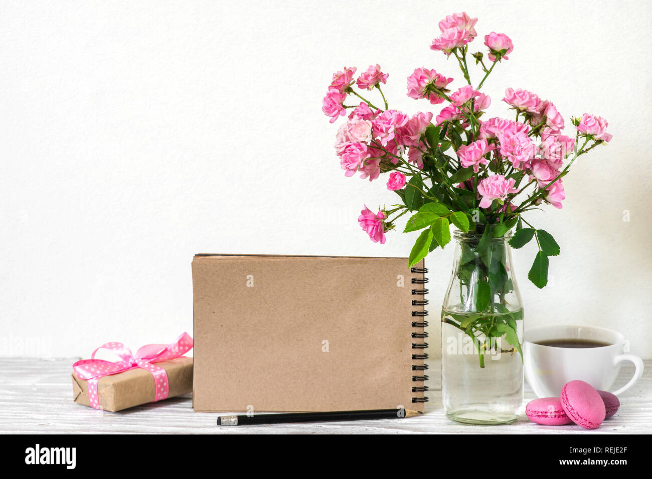 Schönen Blumenstrauß aus Rosen Blumen, Kaffeetasse, Makronen, Geschenkbox und Leere hipster Notebook mit Platz für Text. Urlaub oder Hochzeit Hintergrund Stockfoto