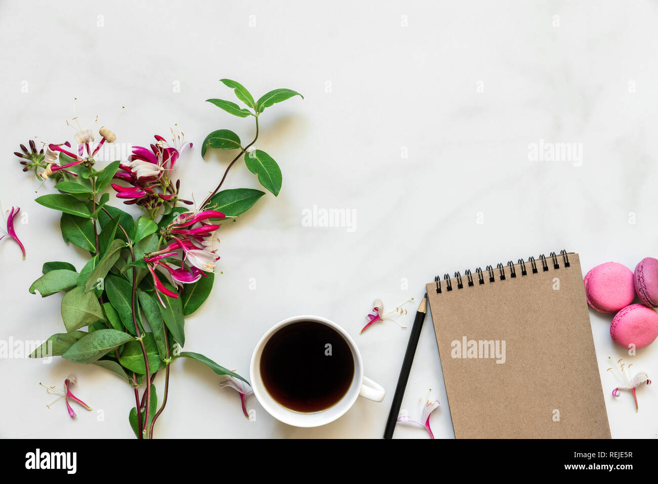 Kreative Gestaltung aus geißblatt Blumen Blumenstrauß, Kaffeetasse, leer Notebook und Makronen mit weißem Marmor tisch mit Kopie Raum. top anzeigen. Mock Stockfoto