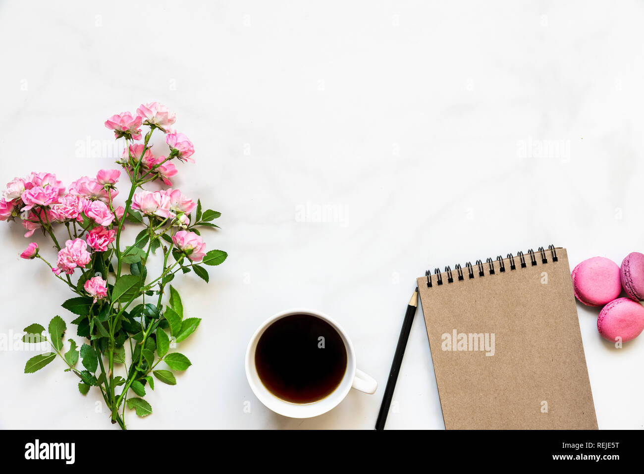 Kreative Gestaltung aus rosa Rose blumen blumenstrauss, Kaffeetasse, leer Notebook und Makronen mit weißem Marmor tisch mit Kopie Raum. top anzeigen. Mock up Stockfoto