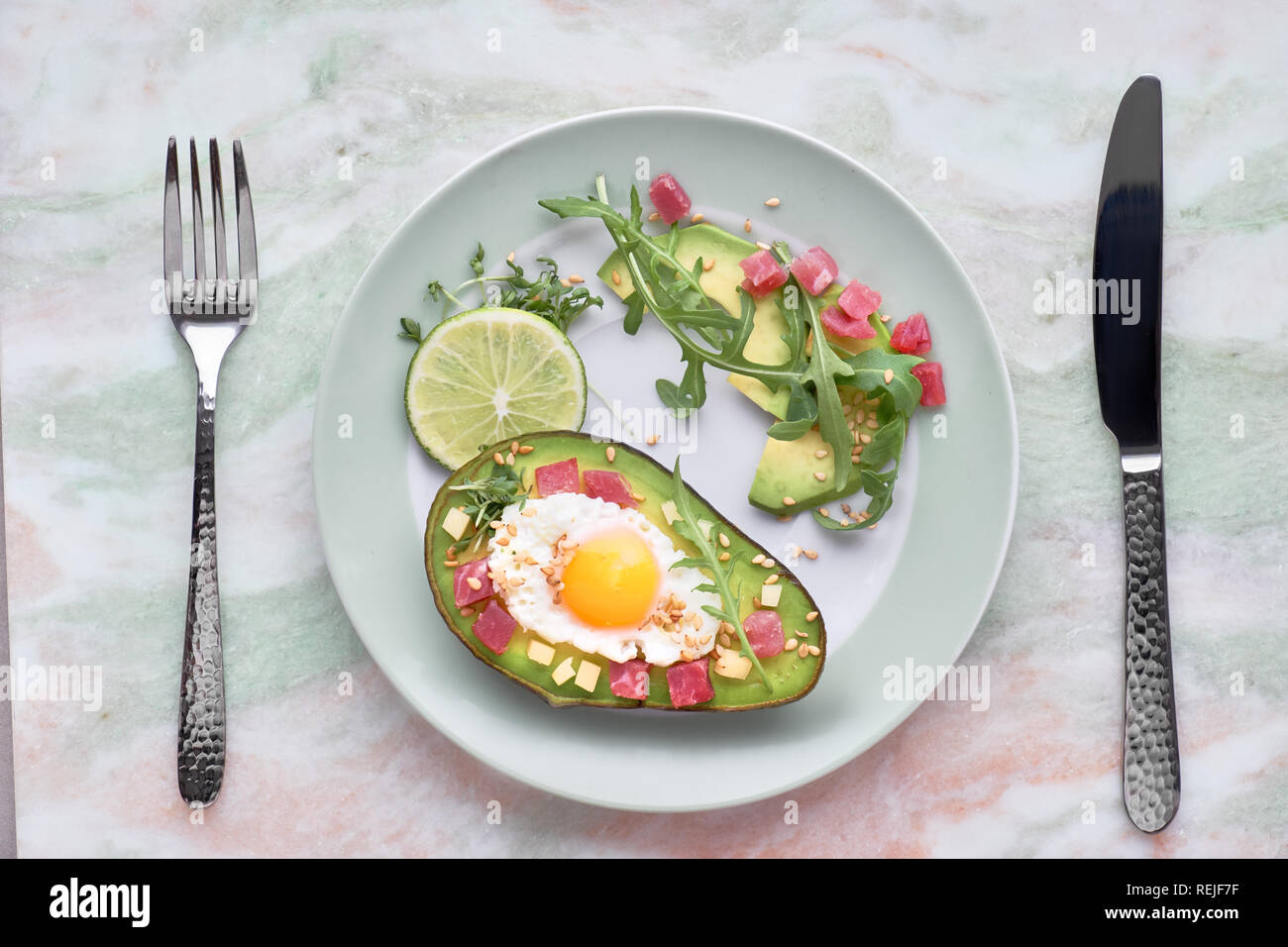 Keto Diät Teller: gebackene Avocado Boot mit Schinken würfeln, Wachtel Ei und Käse mit grünen Rucola Salat serviert. Stockfoto