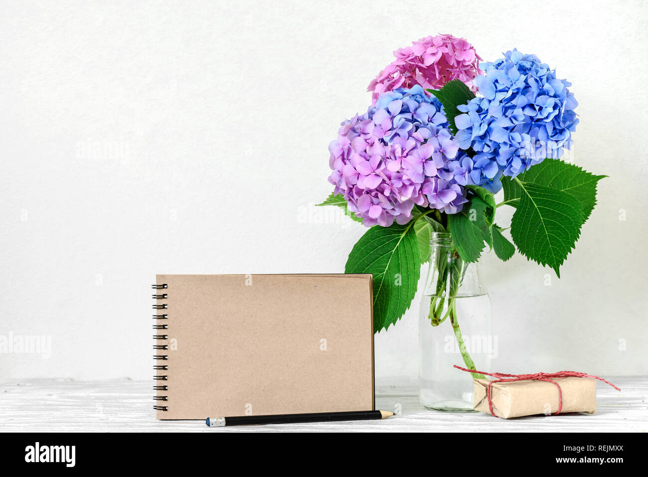 Kreative mock up mit einem schönen Blumenstrauß aus Rosa und Blaue Hortensie Blumen, Geschenkbox und Leere hipster Notebook mit Platz für Text. Urlaub oder wedd Stockfoto