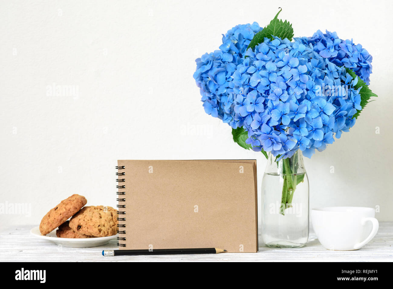 Kreative mock up mit einem schönen Blumenstrauß Blaue Hortensie Blumen, Kaffee Tasse, Hafer Cookies und leeren hipster Notebook mit Platz für Text. Holiday o Stockfoto