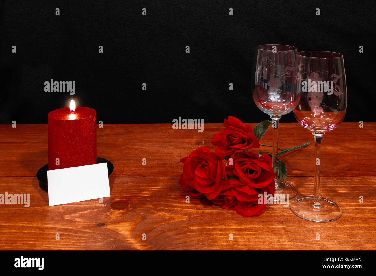 Schöne geätzt Weingläser mit roten Rosen und rote Kerze auf Holztisch und dunklen Hintergrund. Valentinstag, Muttertag, Ostern, Weihnachten, Hochzeit C Stockfoto