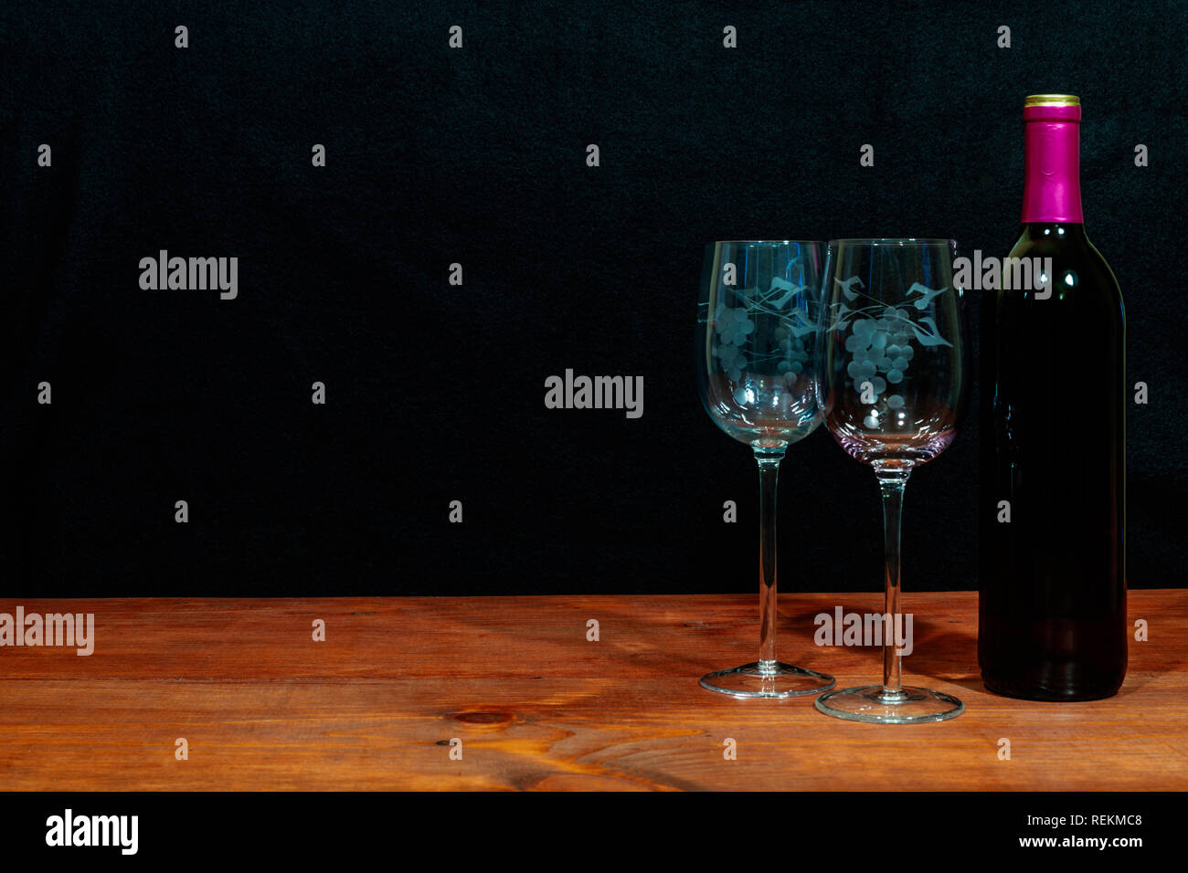 Schöne geätzte Gläser und eine Flasche Rotwein auf dem Tisch und dunklen Hintergrund. Valentinstag, Muttertag, Ostern, Weihnachten, Hochzeit Konzepte Stockfoto