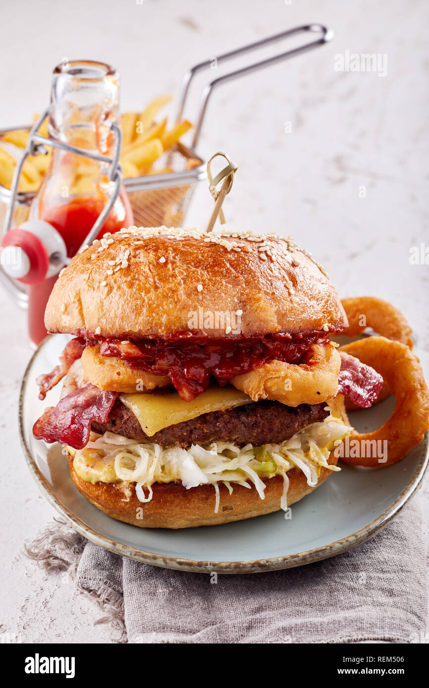 Pattie mit Zwiebelringen Burger mit frittierte Tintenfischringe, knusprigem Speck, Käse und ein Rindfleisch Patty mit Pommes frites serviert. Stockfoto