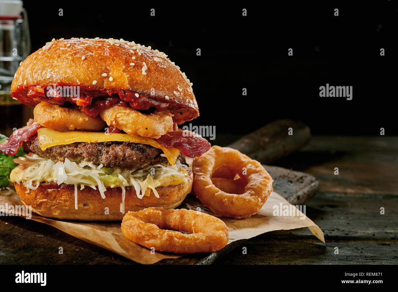 Gourmet Surf and Turf Burger mit Tintenfischringe, knackigen Speck, Rindfleisch Patty und Käse serviert auf einem rustikalen Holzbrett über einen dunklen Hintergrund mit Kopie spa Stockfoto