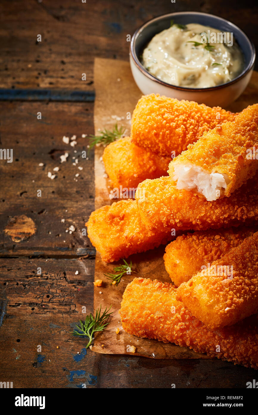 Knusprige Fischstäbchen oder Stöcke in gebraten oder im Ofen gebackene  Brotstückchen auf braunem Papier auf einem rustikalen Tisch serviert mit  einem Tartar Soße Stockfotografie - Alamy