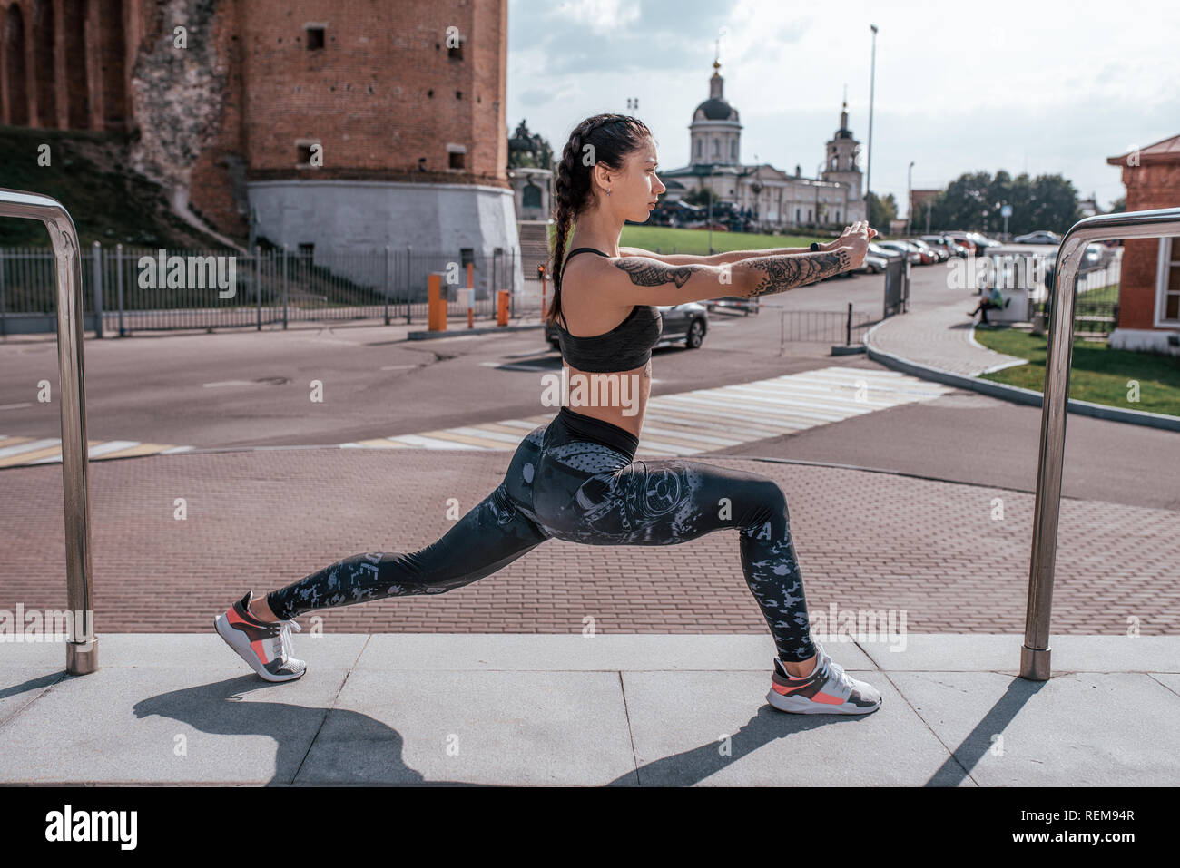 Athlet Mädchen tun stretching Muskeln vor dem Joggen am Morgen in der Stadt. Erwärmt den Körper, Beinmuskulatur. Das Konzept einer gesunden Lebensweise. Gebräunte Haut und Tätowierungen. Stockfoto
