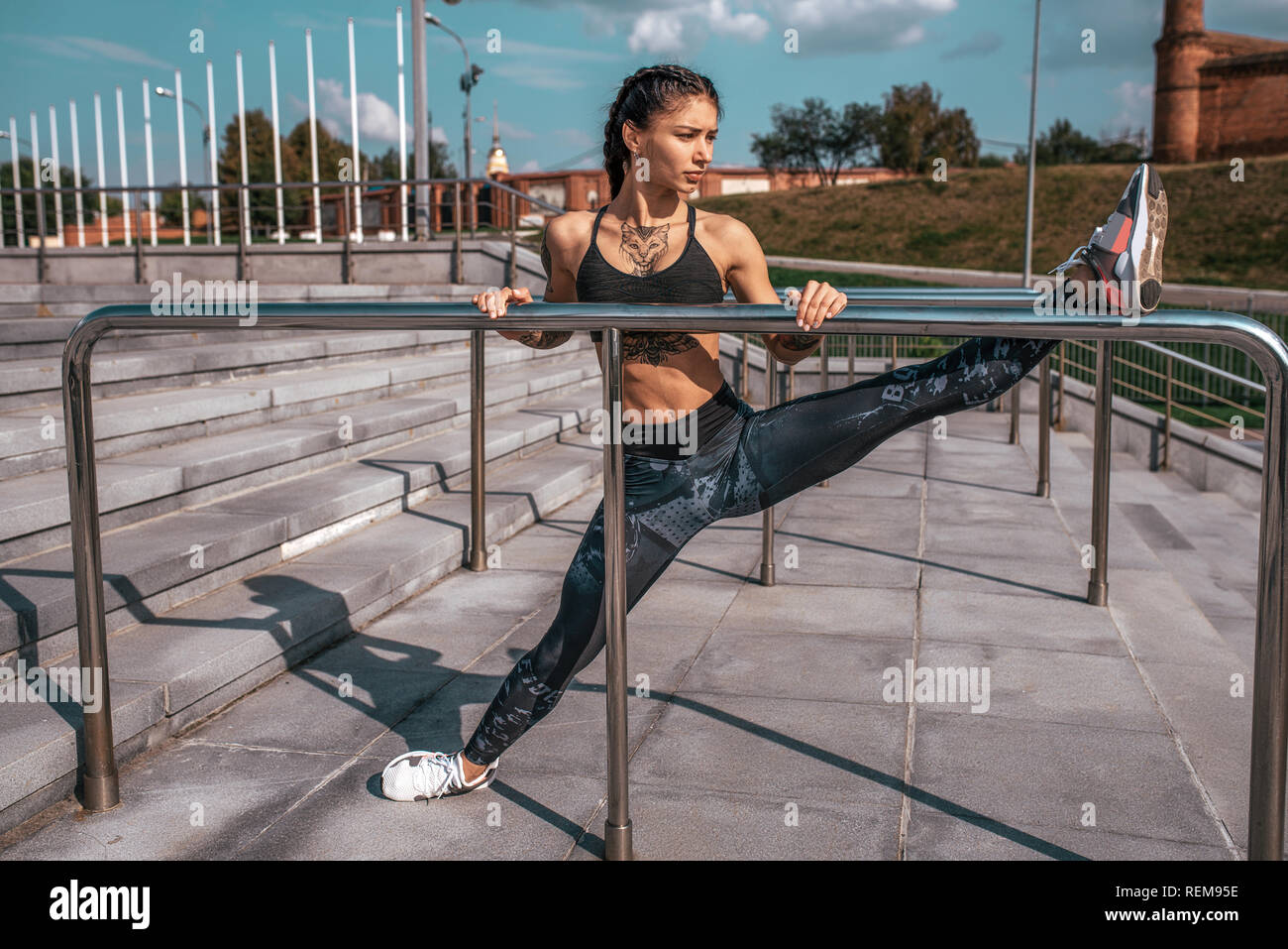 Mädchen Athlet macht stretching Muskeln der Beine, vor dem Joggen am Morgen in die Stadt. Macht Gymnastik auf piril. Das Konzept einer gesunden Lebensweise. Bei GARN-Sitzen. Gebräunte Haut und Tätowierungen. Stockfoto