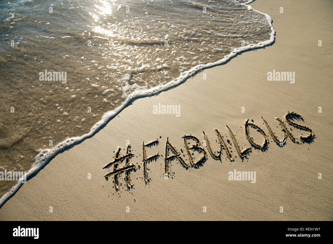 Fabelhaft, die modischen Schlagwort mit einem modernen social media Hashtag handschriftlich auf einem glatten Sandstrand mit ankommenden Welle Stockfoto