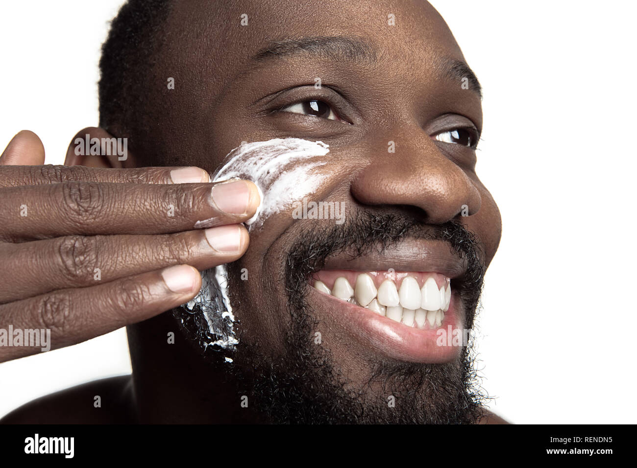 Junge afrikanische amerikanische Kerl Anwendung Gesicht Creme unter den Augen auf weißem Hintergrund. Portrait einer jungen Glücklich lächelnde afrikanischer Mann im Studio. High Fashion männliches Modell. Stockfoto