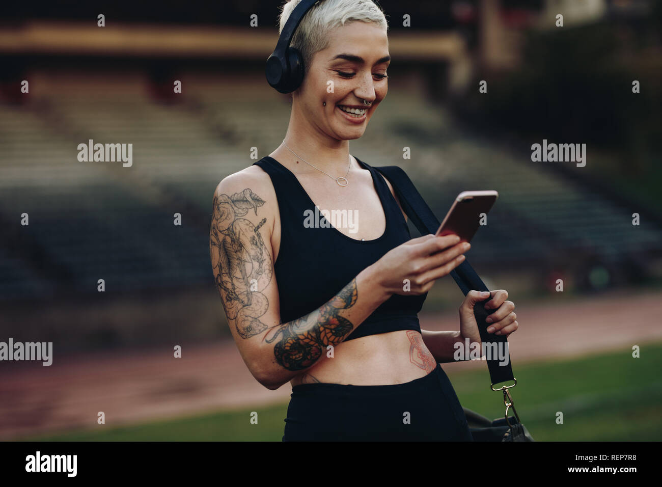 Happy fitness Frau mit Handy stehen in einem Leichtathletik Stadion. Frau in Fitness Kleidung Musik auf kabellosen Kopfhörern stehen Stockfoto