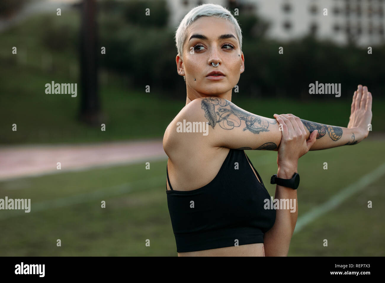 Sportlerin mit Tattoo auf dem Arm zu tun Stretching Übungen in einer Masse. Porträt einer Frau, die in der Fitness Kleidung, Warm-up Übungen. Stockfoto