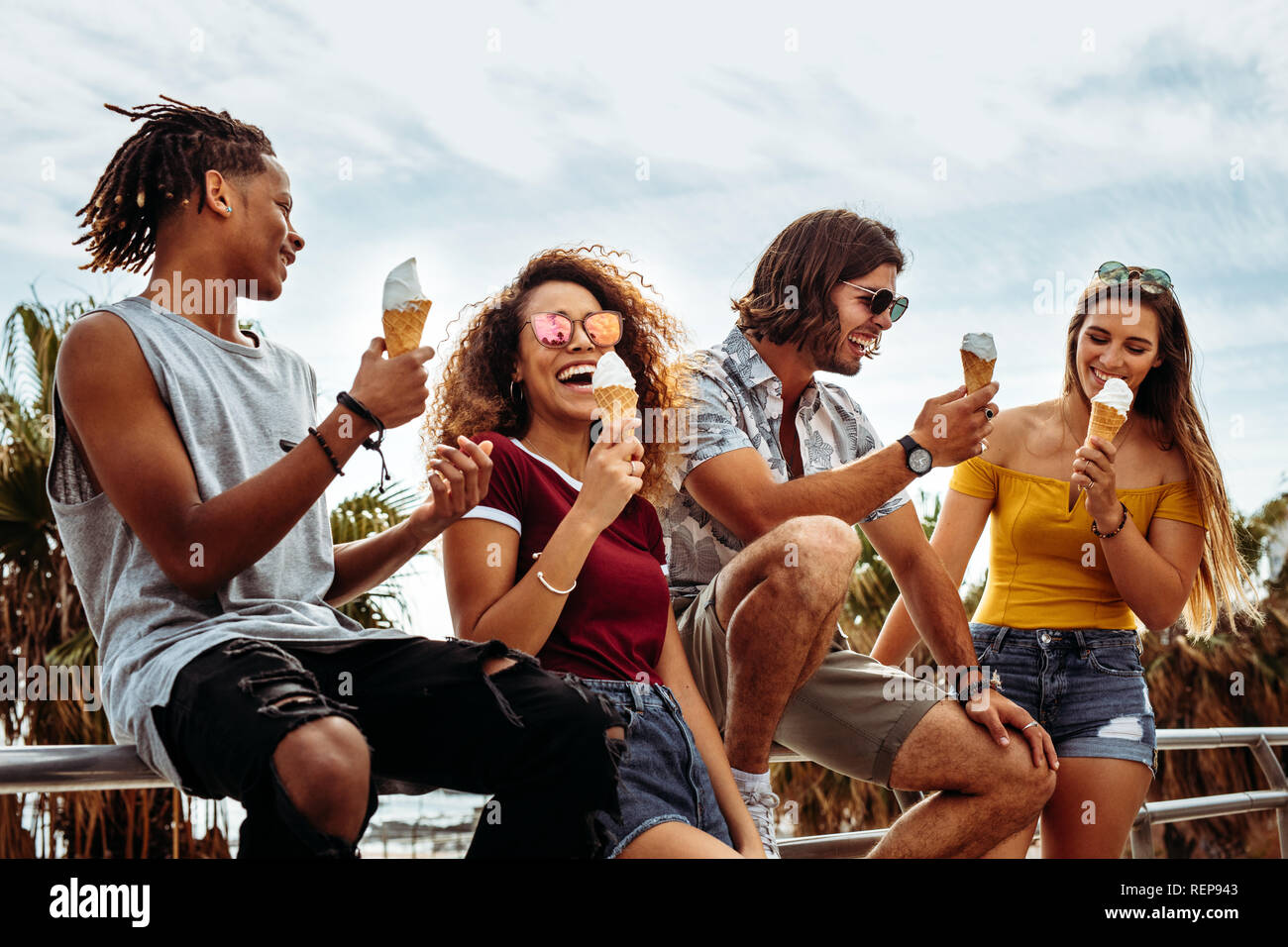 Multi-ethnischen Gruppe genießen Eis essen im Freien durch ein Geländer. Lächelnde junge Männer und Frauen essen Eis im Freien. Stockfoto