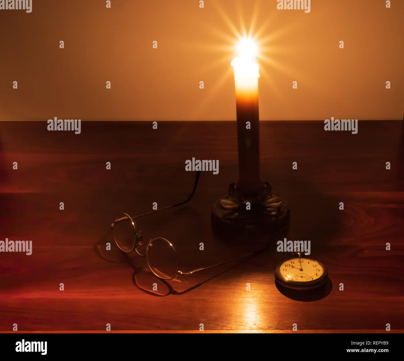 Ein reichhaltiges, Nussbaum dunkel Desktop mit einer brennenden Kerze, alte Taschenuhr, und Draht Hornbrille. Stockfoto