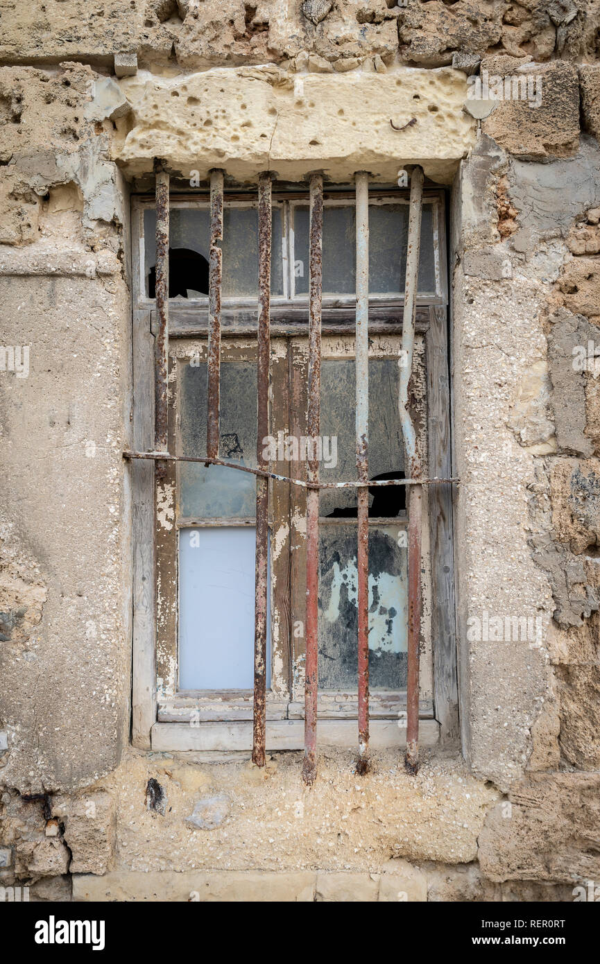 Gebrochene Fenster mit Eisenstangen in einem alten Kalkstein Wand gesetzt. Stockfoto