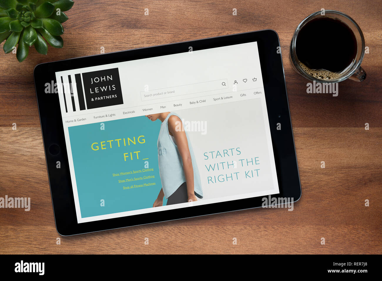 Die Website von John Lewis und Partner auf einem iPad Tablet gesehen wird, auf einen hölzernen Tisch zusammen mit einem Espresso und einem Haus Anlage (nur redaktionell) Stockfoto