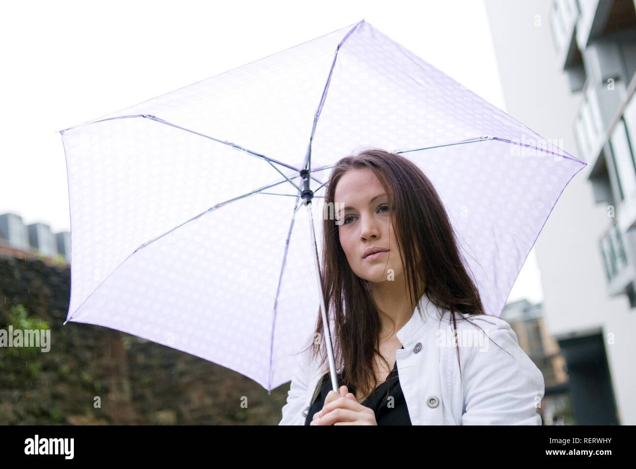 Junge Frau Unterschlupf unter einem Sonnenschirm an einem regnerischen Tag Stockfoto